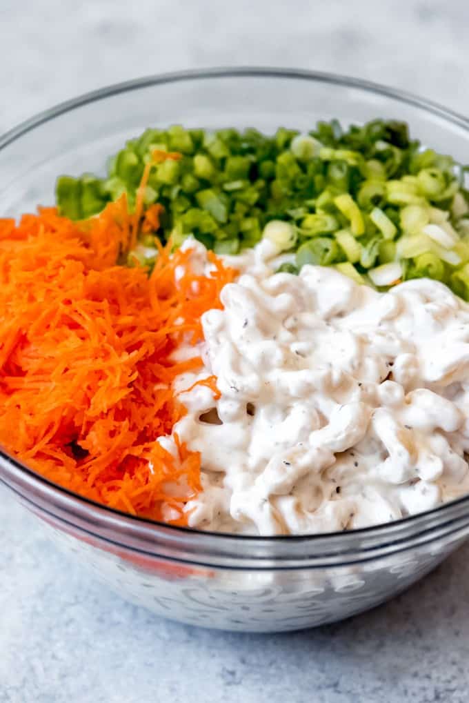An image of a bowl of macaroni noodles coated in a creamy mayo-based dressing with grated carrots, green onions, and celery for macaroni salad.