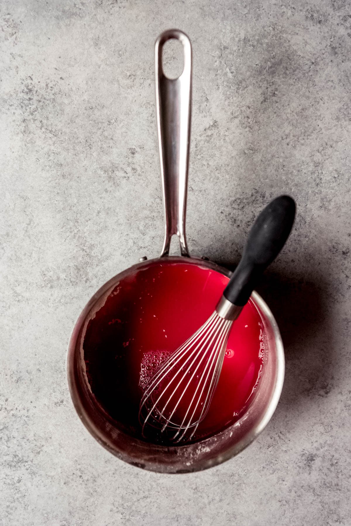 A whisk in a saucepan with sugar, cornstarch, and cherry juice.