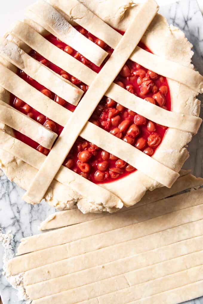 An overhead image showing strips of pie crust being added in a lattice pattern.