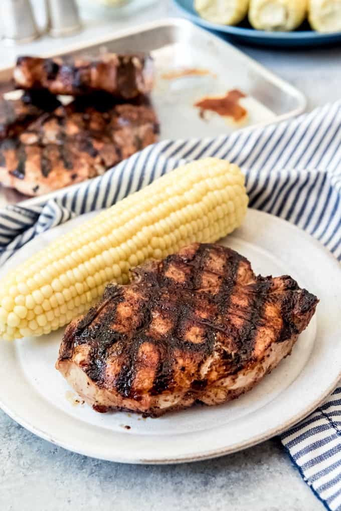 An image of a perfectly juicy grilled pork chop with grill marks on a plate with corn on the cob.