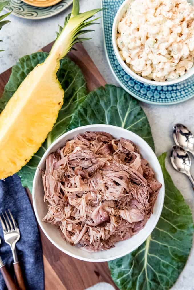 An image of slow cooker kalua pork or kalua pig next to a sliced pineapple and Hawaiian macaroni salad.
