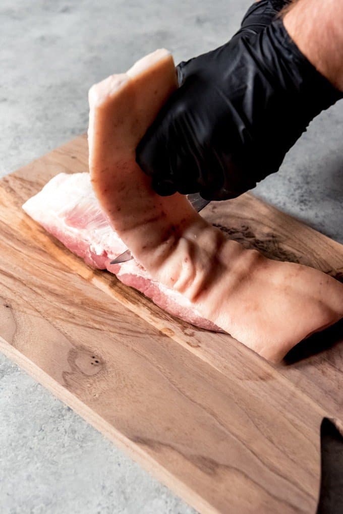 An image of a piece of pork belly being trimmed of the skin and some of the fat.