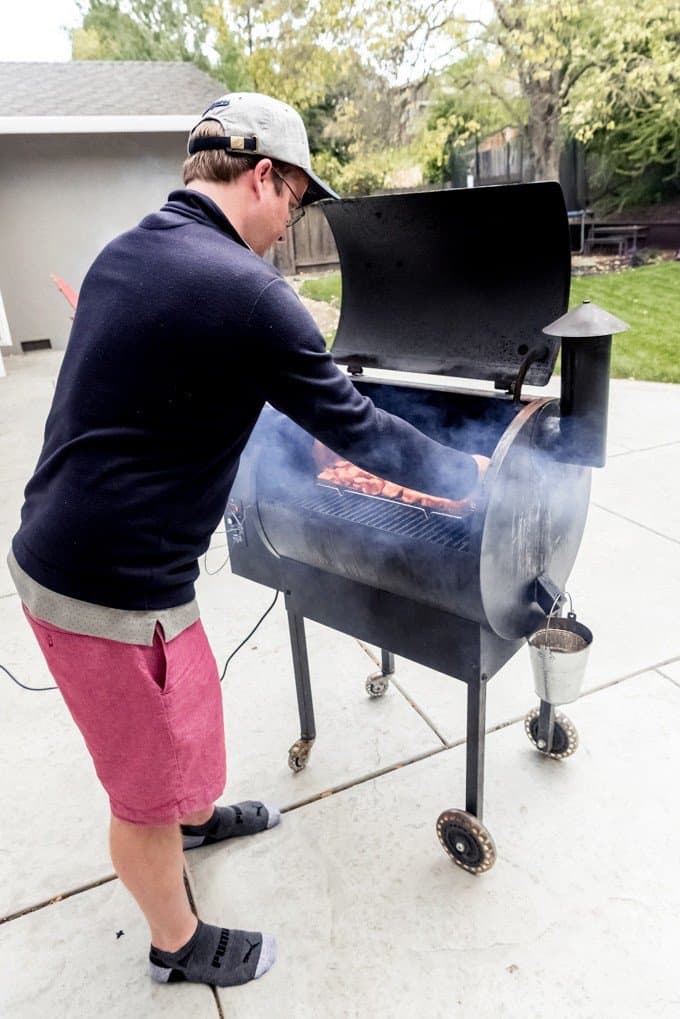 An image of a man putting pork belly on a smoker to make burnt ends.