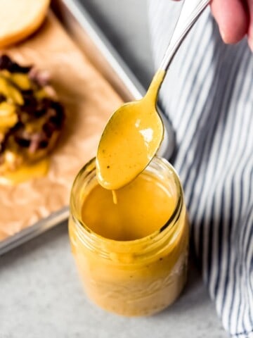 An image of a spoon coated in Carolina mustard BBQ sauce being held over a jar of the sauce.