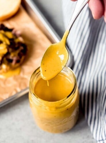 An image of a spoon coated in Carolina mustard BBQ sauce being held over a jar of the sauce.
