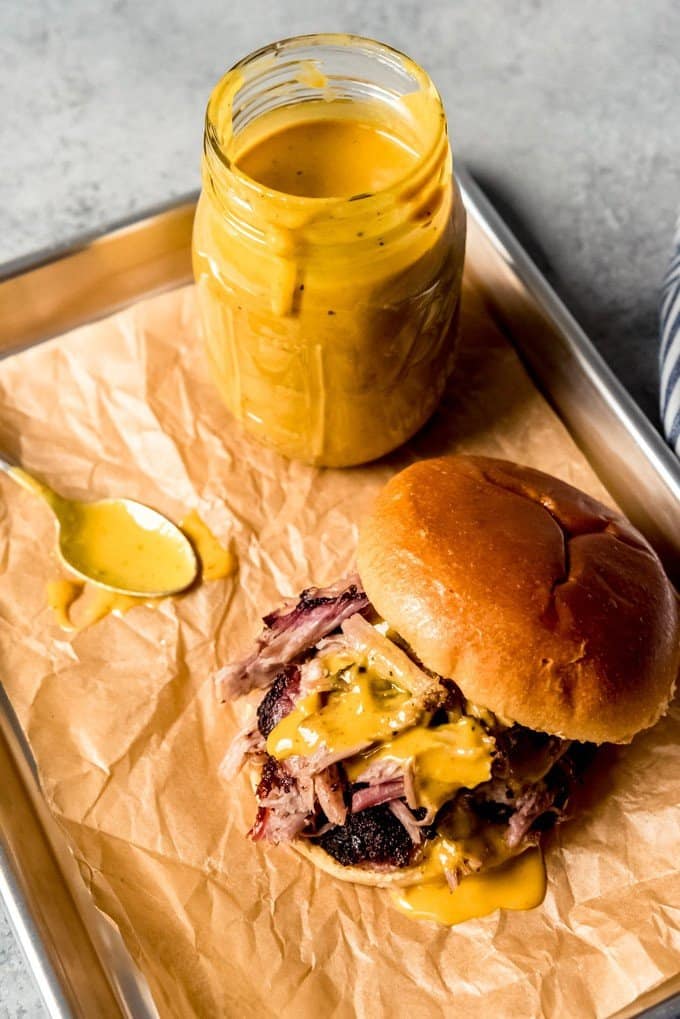 An image of a pulled pork sandwich drizzled with Carolina gold BBQ sauce next to a jar of the sauce.