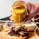 An image of Carolina gold BBQ sauce being poured over pulled pork on a bun.