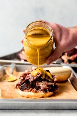 An image of Carolina gold BBQ sauce being poured over pulled pork on a bun.