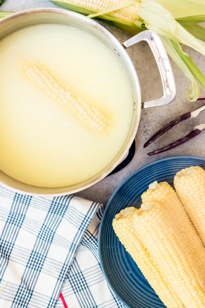 An image of corn on the cob being cooked in a pot of water, milk, and butter.