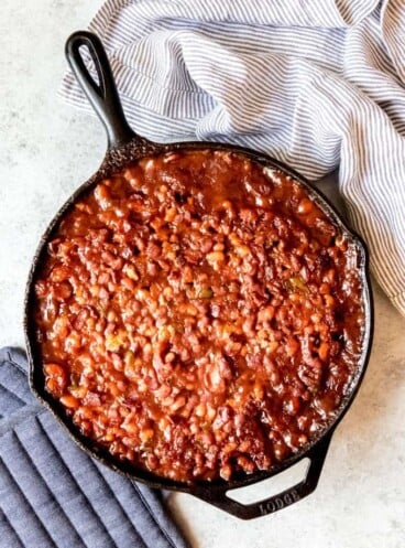 An image of a large cast iron skillet filled with potluck baked beans.