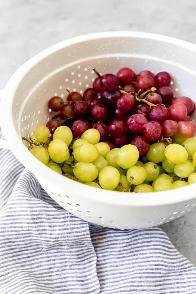 An image of a white colander filled with red and green grapes that have just been washed for grape salad.