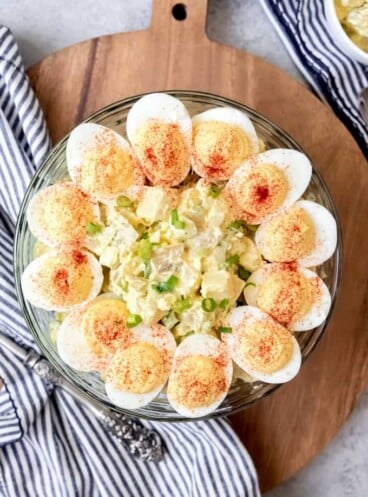 a ring of garnished deviled eggs around the top of a bowl full of deviled egg potato salad
