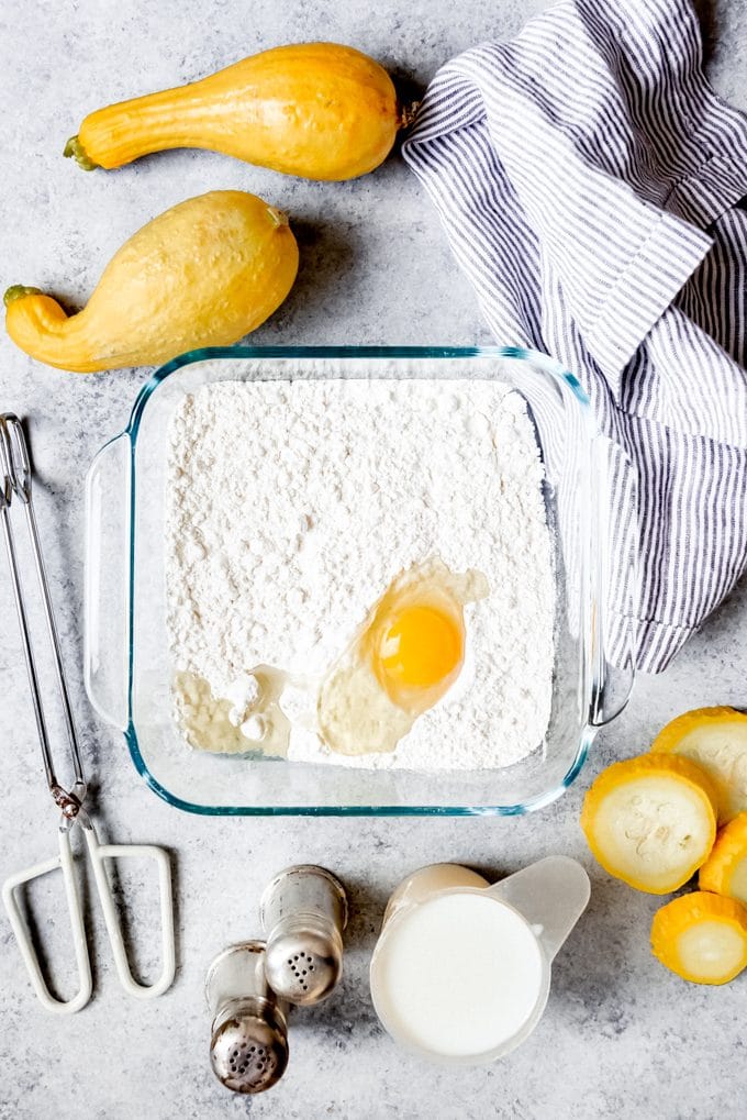 egg in flour mixture in baking dish sourrounded by other ingredients and tools needed