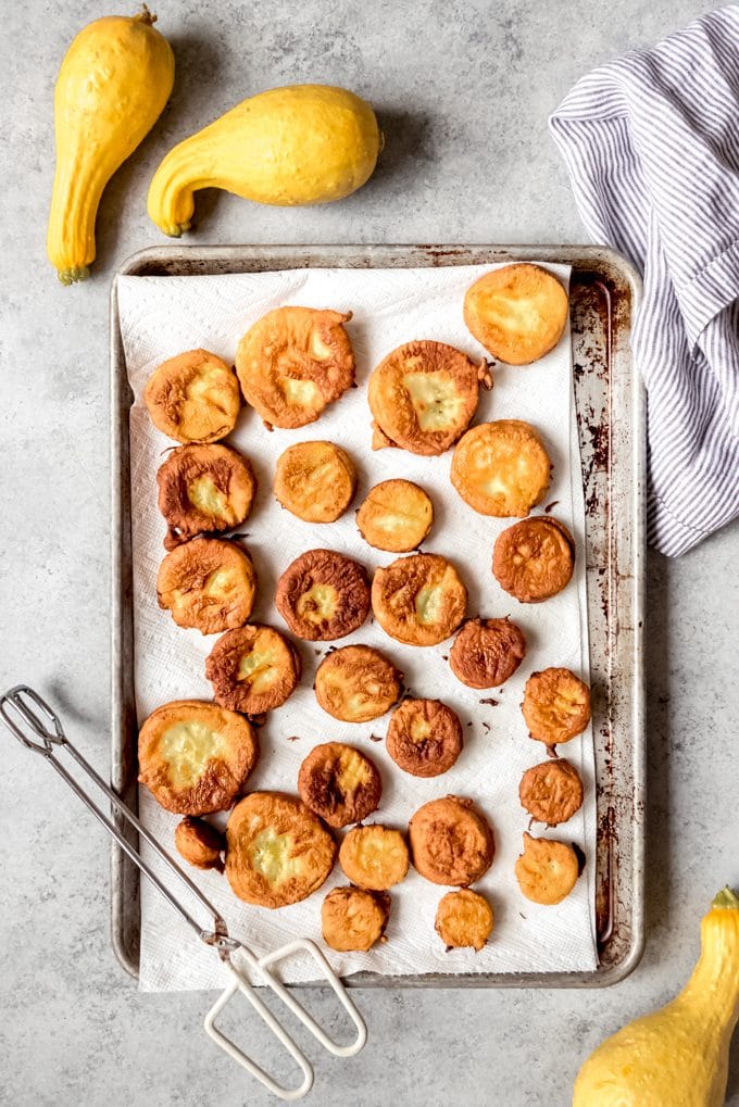a baking sheet full of fried yellow squash and a pair of tongs resting on it