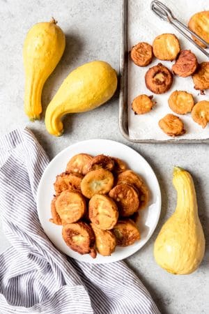 a stack of fried yellow squash on a plate with more squash whole and fried around it