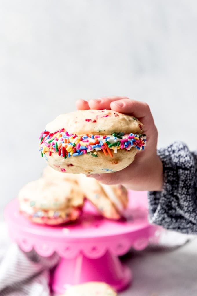 An image of a hand holding a funfetti whoopie pie with sprinkles around the edges.