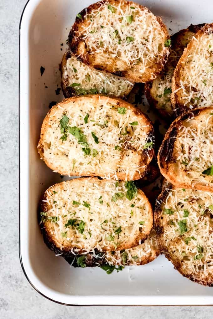 An image of slices of grilled garlic bread topped with Parmesan cheese and chopped parsley.