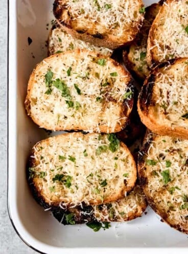 An image of slices of grilled garlic bread topped with Parmesan cheese and chopped parsley.