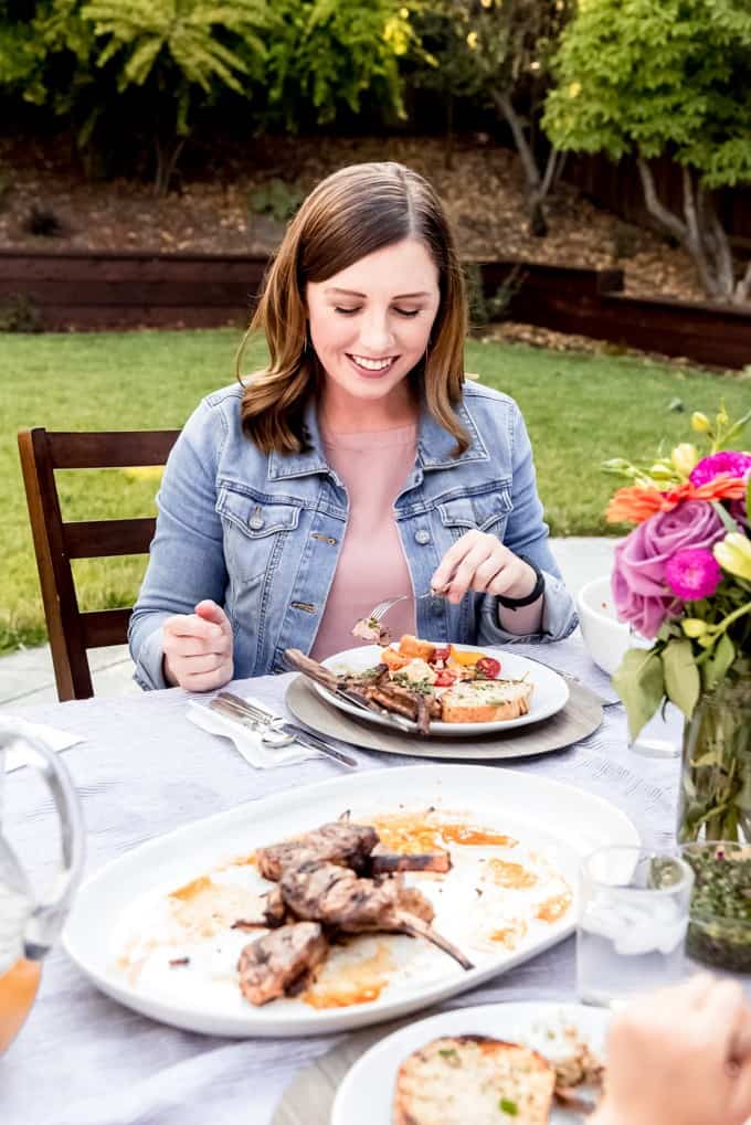 An image of a woman eating grilled lamb chops at an outdoor dining event.