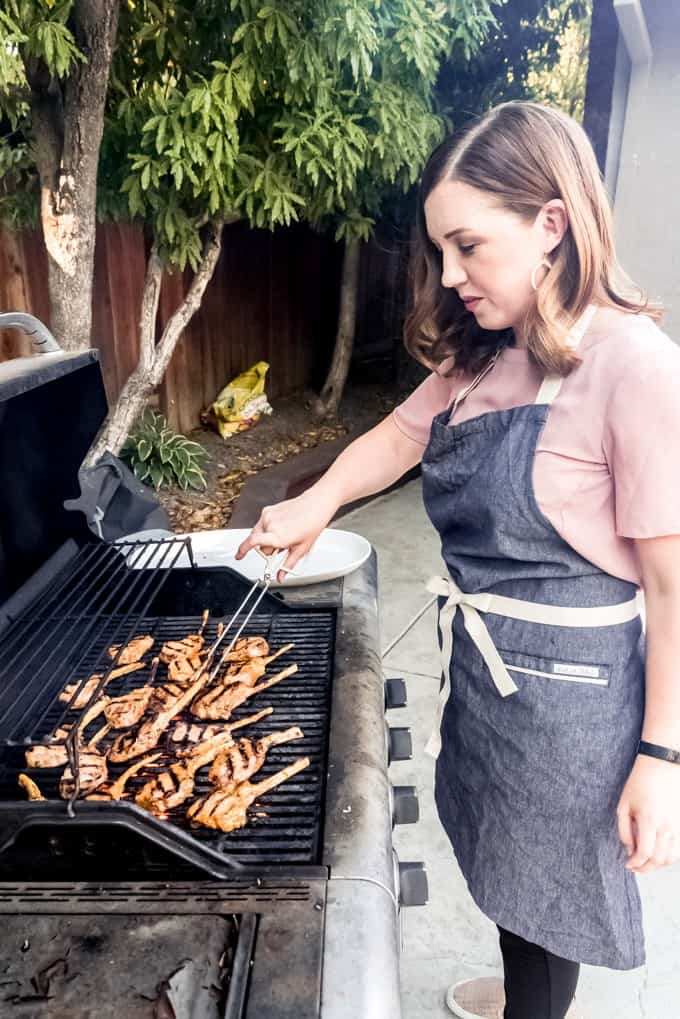 An image of a woman turning lamb chops on the grill.
