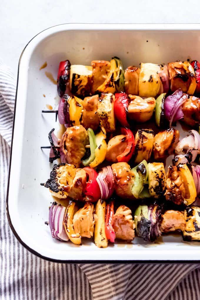 An image of lightly charred pineapple, vegetables, and chicken on skewers after being brushed with a teriyaki glaze.