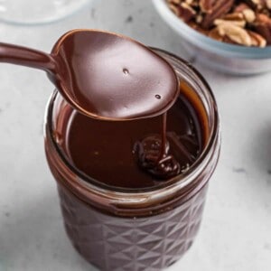 A spoon drizzling homemade hot fudge sauce into a glass jar.