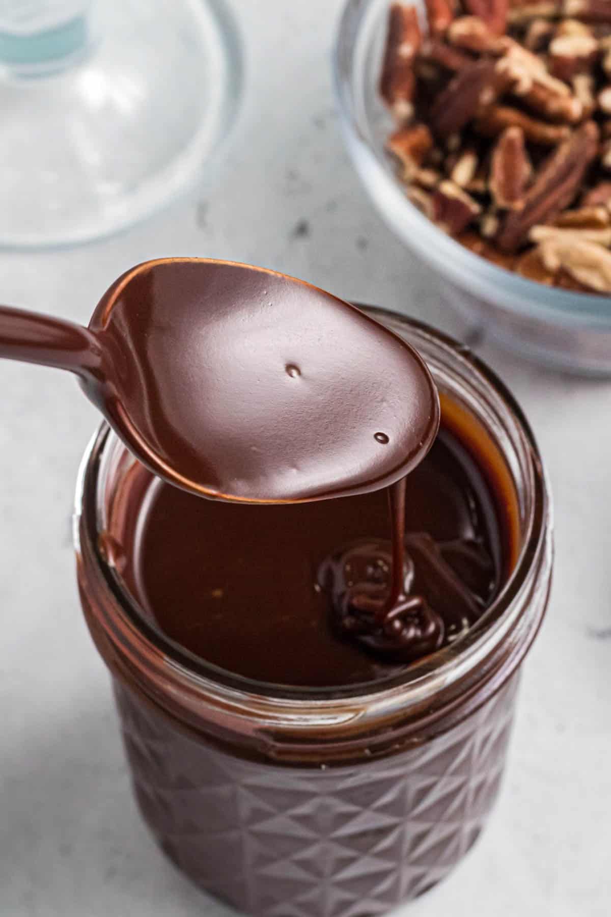 A spoon drizzling homemade hot fudge sauce into a glass jar.