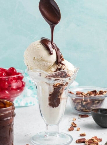 A spoon drizzling homemade hot fudge sauce onto scoops of vanilla ice cream.