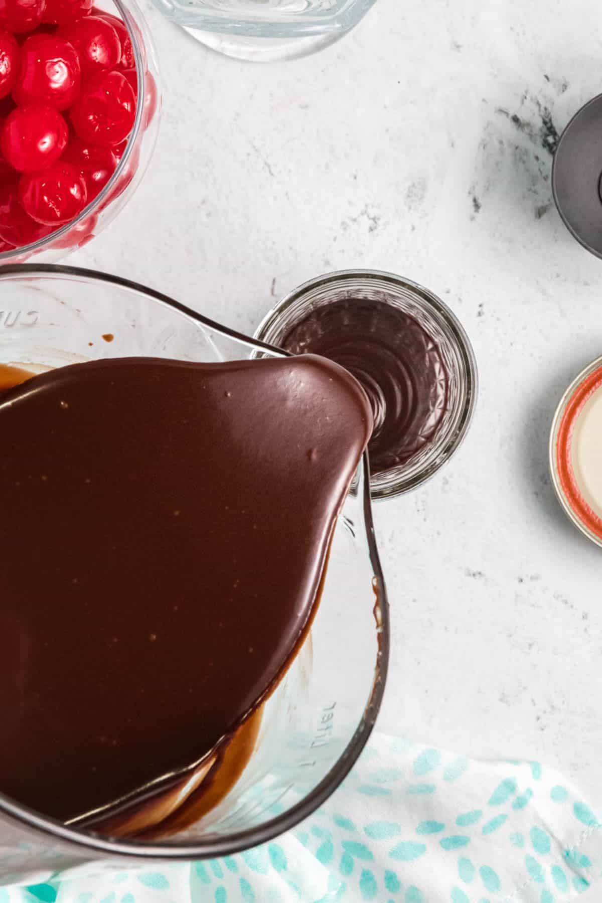 Pouring thick hot fudge sauce into a glass jar for storage.