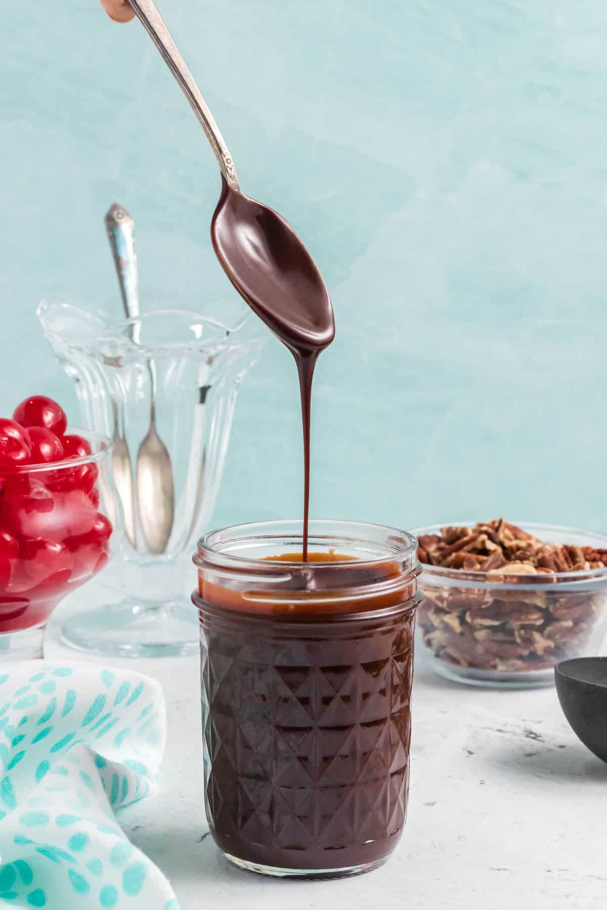 A spoon lifted over a jar of homemade hot fudge.
