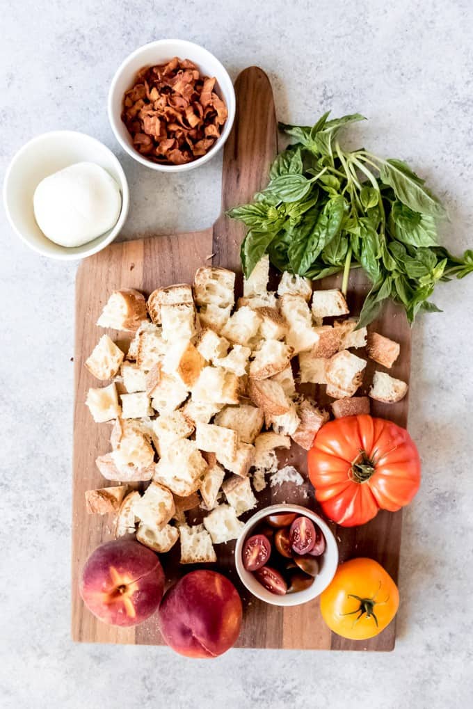 An image of a cutting board piled with the ingredients for peach panzanella salad.