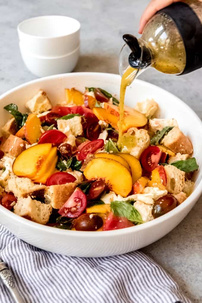 An image of a simple, homemade honey dijon vinaigrette being poured over a peach panzanella salad.