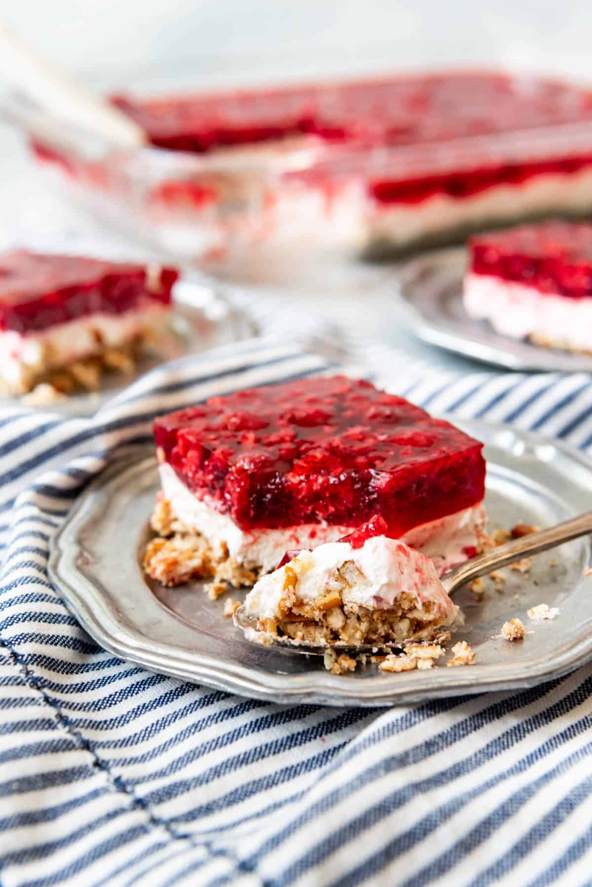 A slice of raspberry pretzel salad on a plate with a bite taken out of it.