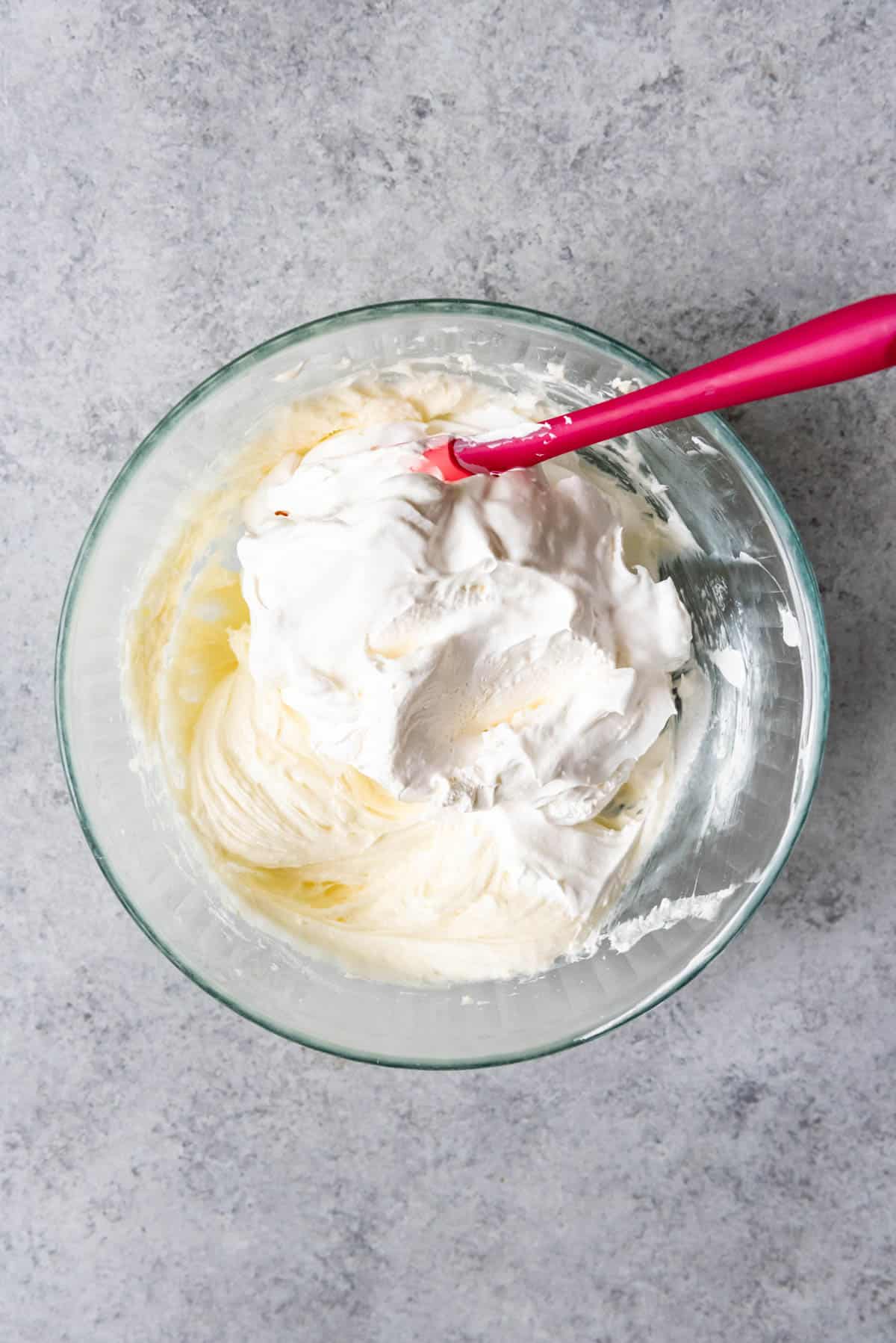 An image of Cool Whip being folded into a cream cheese and sugar mixture for the creamy layer in raspberry pretzel salad.