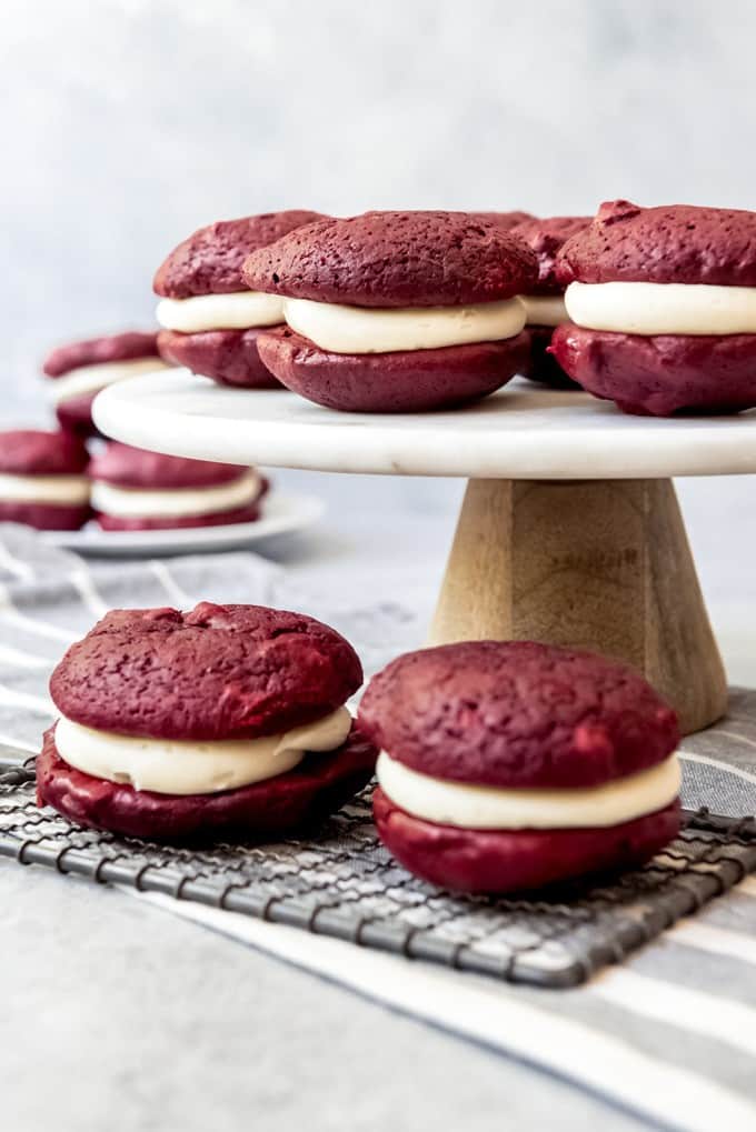 An image of red velvet whoppie pies on a cake stand and wire cooling rack.