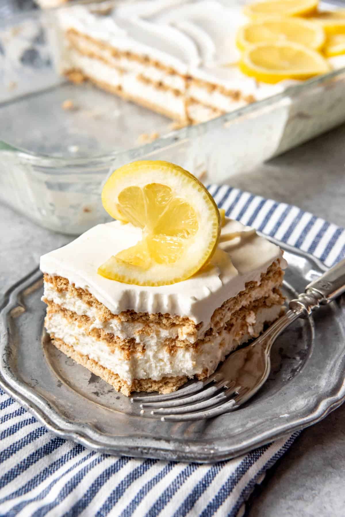 An image of a piece of lemon icebox cake with a lemon slice on top for decoration and a bite taken out of the cake.