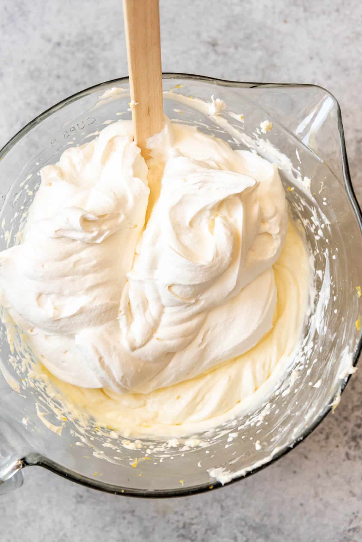 An image of whipped cream being folded into a lemon cream cheese mixture to make the filling for a no-bake dessert.