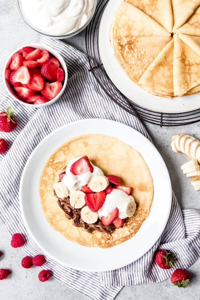 An image of a crepe with nutella, bananas, strawberries, and whipped cream on a plate.