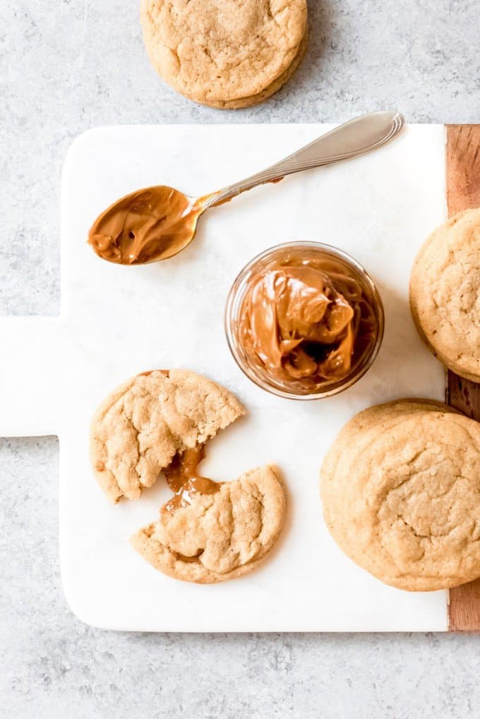 An image of a brown sugar cookie filled with dulce de leche next to a jar of dulce de leche.