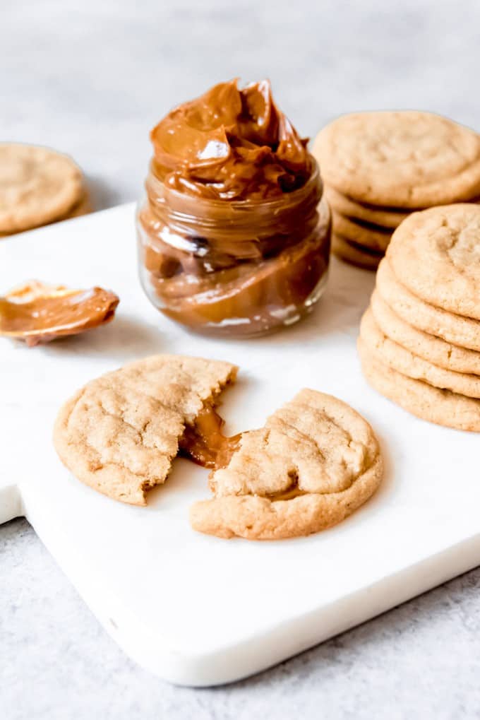 An image of a brown sugar cookie stuffed with dulce de leche that has been pulled apart with caramel spilling out.