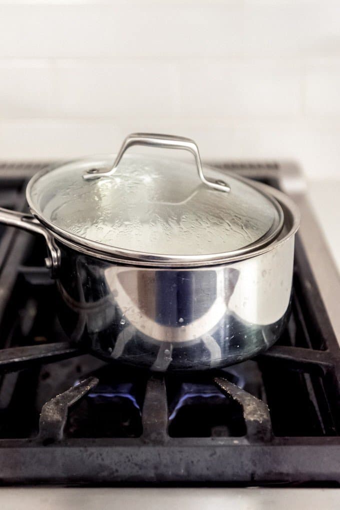 An image of a saucepan with a tilted lid to let steam escape from sticky rice while it cooks.