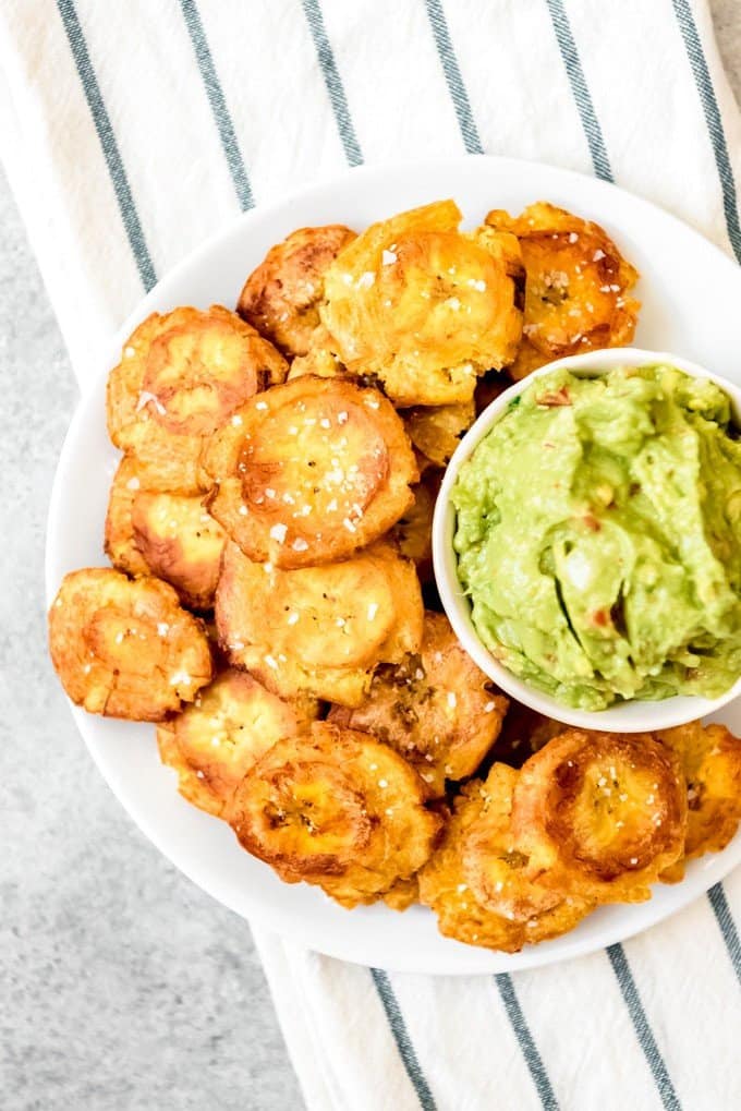 An image of a plate of golden yellow patacones with guacamole for dipping.