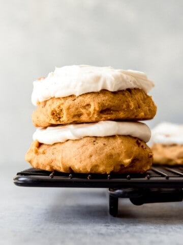 An image of pumpkin cookies with cream cheese frosting stacked on top of each other.