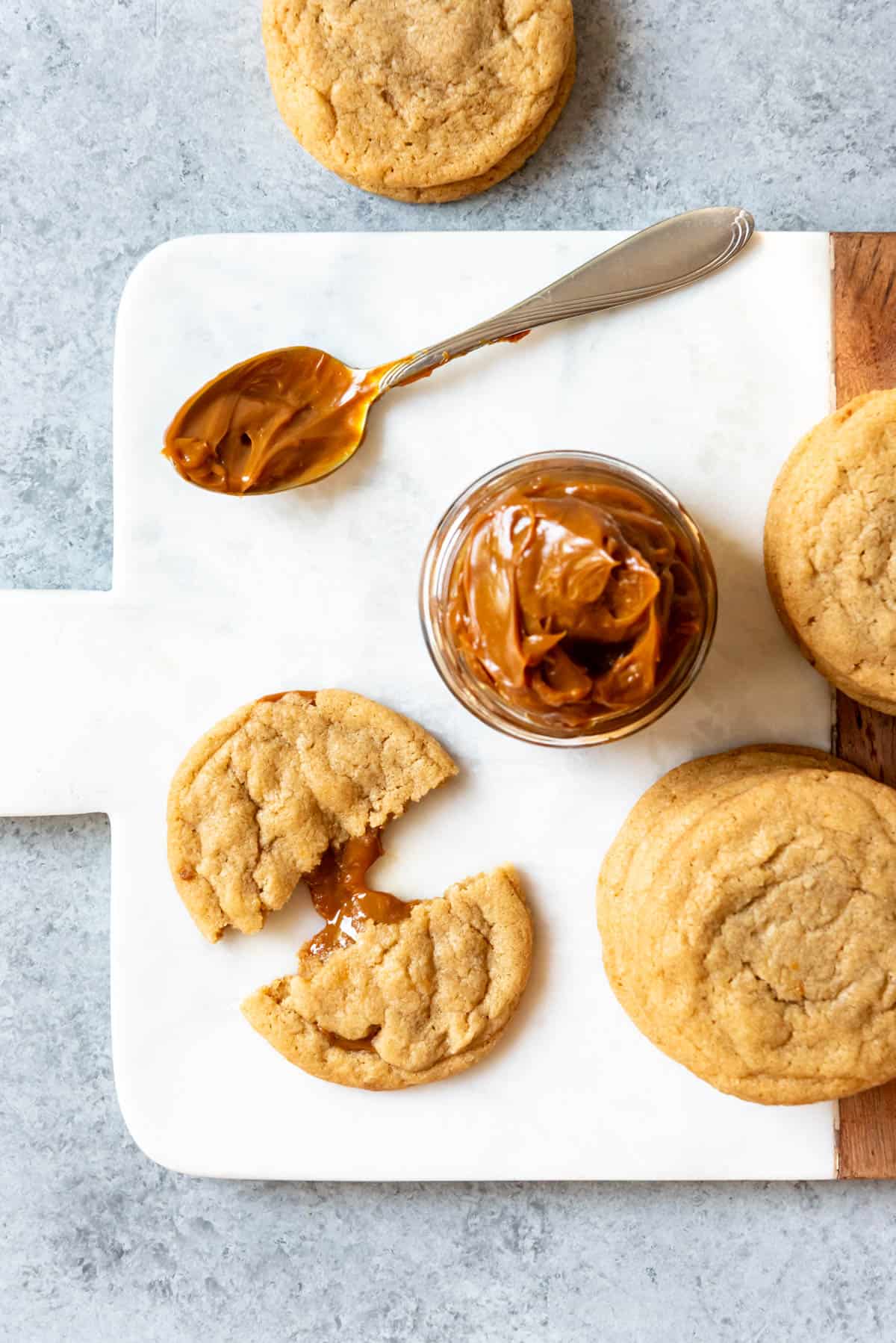 An image of a brown sugar cookie filled with dulce de leche next to a jar of dulce de leche.