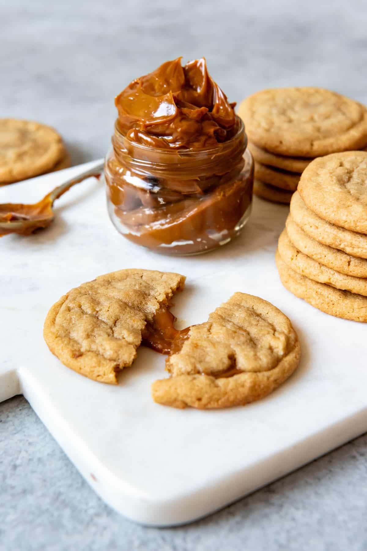 An image of a brown sugar cookie stuffed with dulce de leche with a jar of dulce de leche behind it.