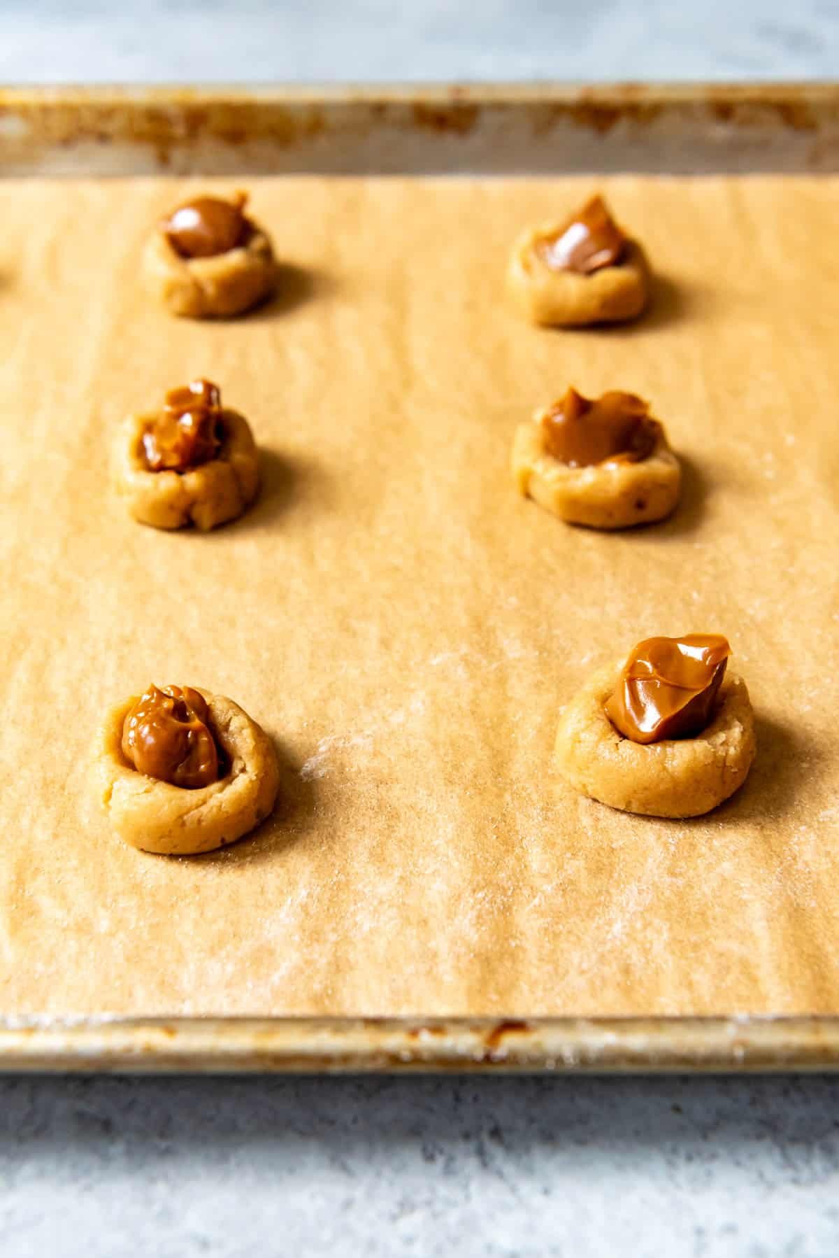 An image of balls of brown sugar cookie dough with dulce de leche spoon on top.