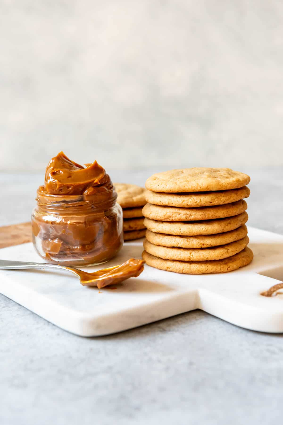 An image of cookies stacked on top of each other next to a jar of dulce de leche.