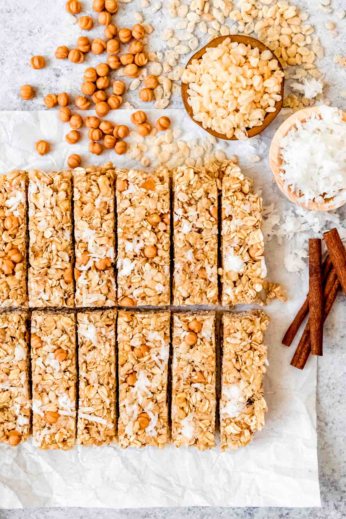 An image of homemade caramel cinnamon coconut krispie granola bars arranged on a surface with spilled ingredients next to them.