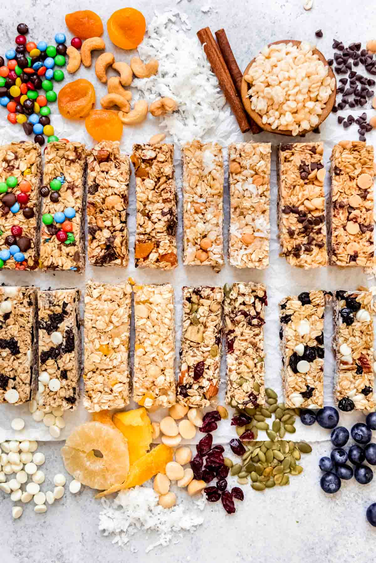 An image of 8 different flavors of homemade granola bars surrounded by granola bar ingredients.