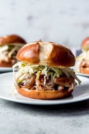 An image of a pulled chicken sandwich made in the slow cooker with a pretzel bun, apple barbecue sauce, and an apple cabbage slaw.